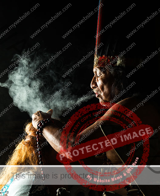 Shaman blows smoke over head of a woman, background is dark