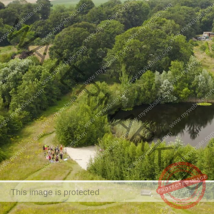 The swimming pond and private beach from birds-view. A large group of people stands by the private beach.