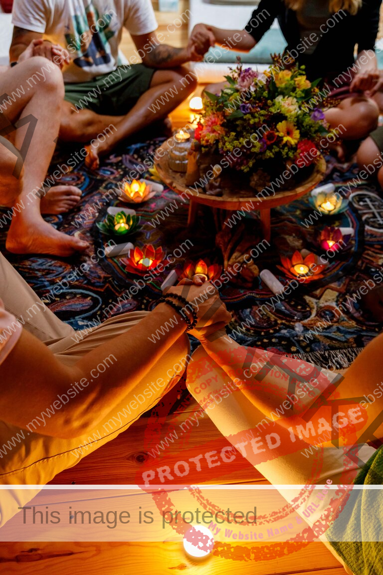 People sitting in a circle and holding hands around candles and a flower
