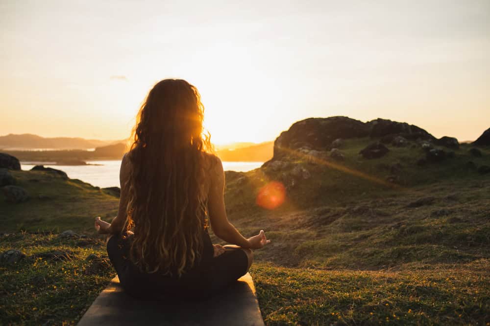 Woman meditating on yoga mat during sunset