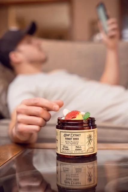 Gummy rings on glas table, man laying on couch, looking on his phone and taking a gummy ring