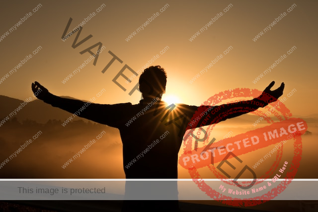 Guy standing on top of a hill while sun rises, clouds and mountains in the background