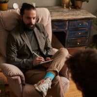 Black haired guy with a notebook talking to another person