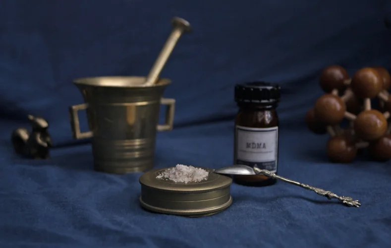 MDMA crystals on steel plate, blue background, jar with MDMA label in the background