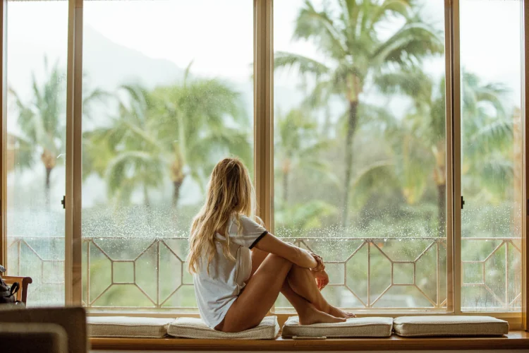 woman sitting in front of large windows looking out into a tropical garden