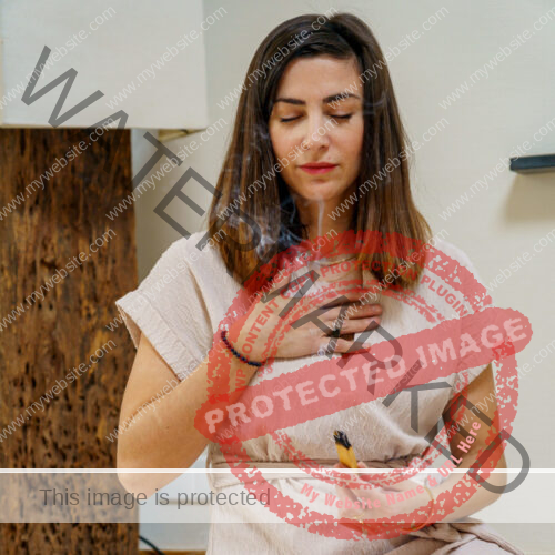 Woman with brown hair, closed eyes holding a hand to her chest and using palo santo