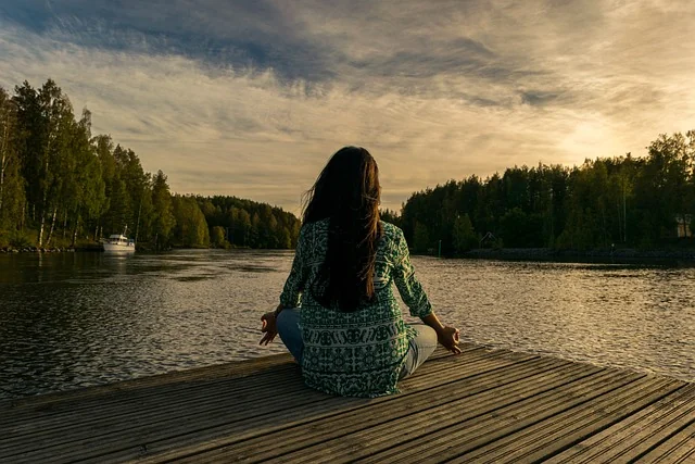Woman meditating on rack, sea, forest and a boat in the background