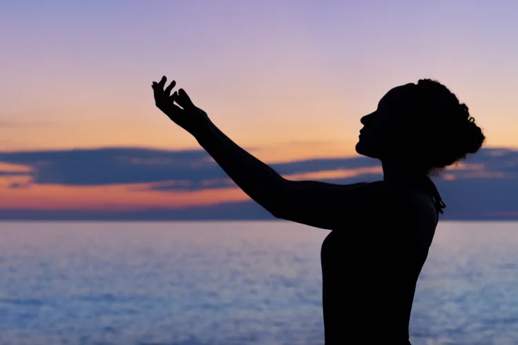 Woman holding arm to the sky during sunset, ocean in the background