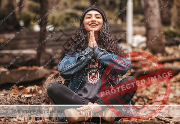 Young woman with brown curly hair meditating and smiling in forest
