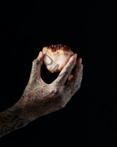 hand holding a crystal, covered in flower of life tattoo