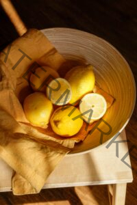 a bowl of lemons with a cloth and sunlight shining on them