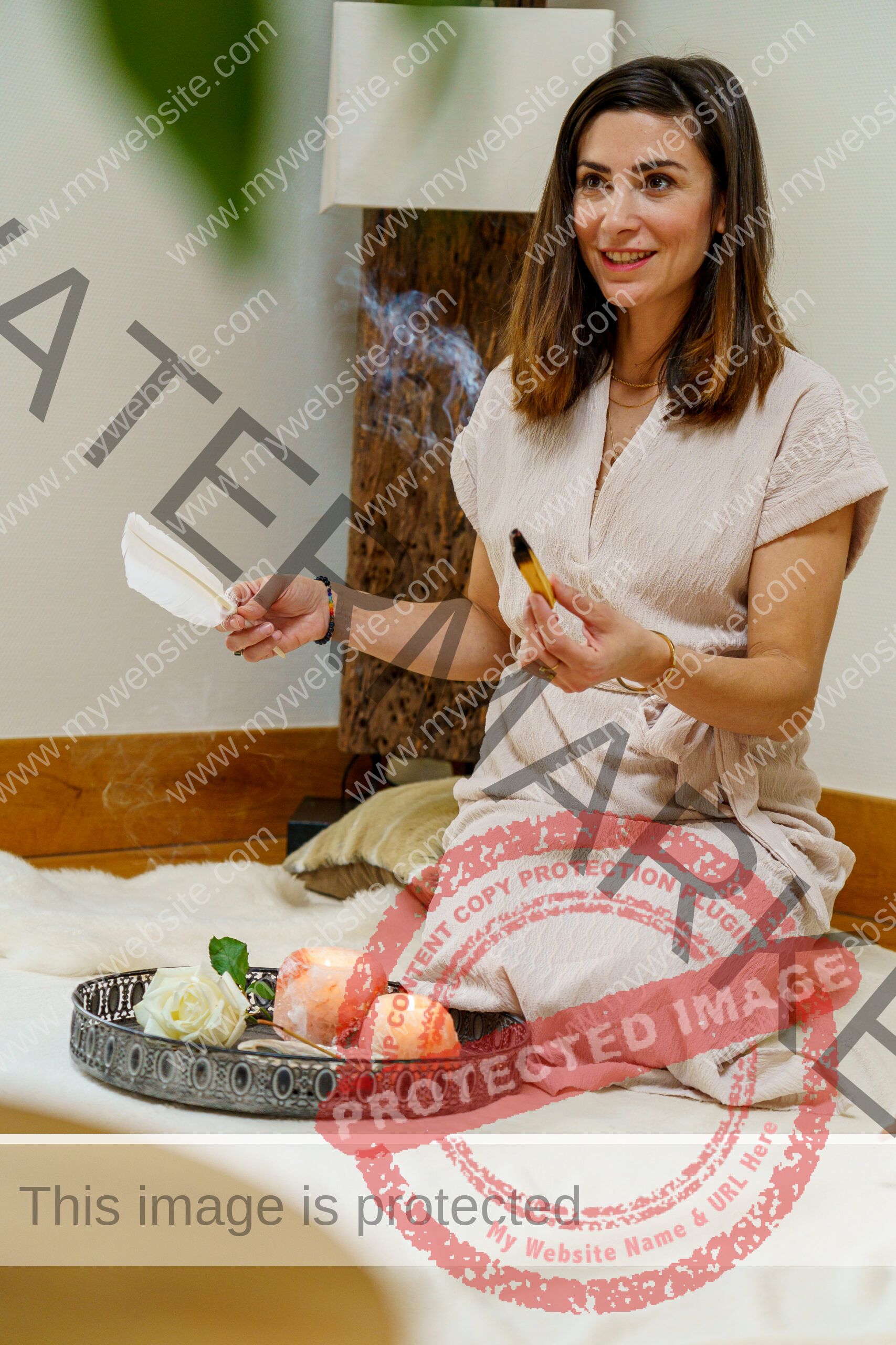 Woman with brown hair holding palo santo wood in her left hand and a white feather in her right hand