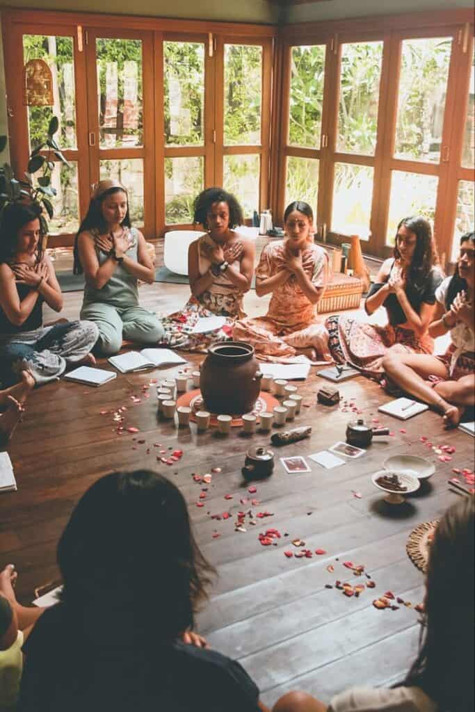 Women circle where every woman is holding her chest with both hands in a natural and brown room with many windows