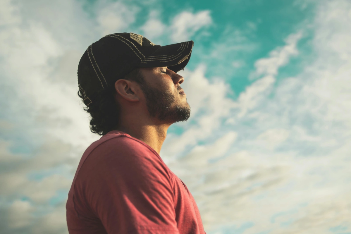 A young guy wearing a black hat with closed eyes, sky with clouds in the background