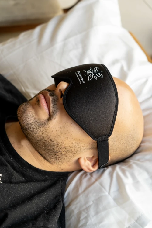 Young man with eye mask laying on white pillow