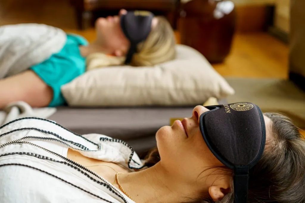 Two woman laying on mattresses with blindfolds
