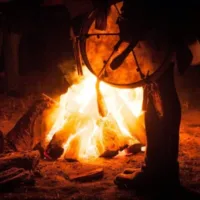 Camp fire, a person with a shamanic drum standing in the foreground