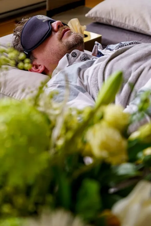 Guy laying on mattress with blindfold, flowers in the foreground