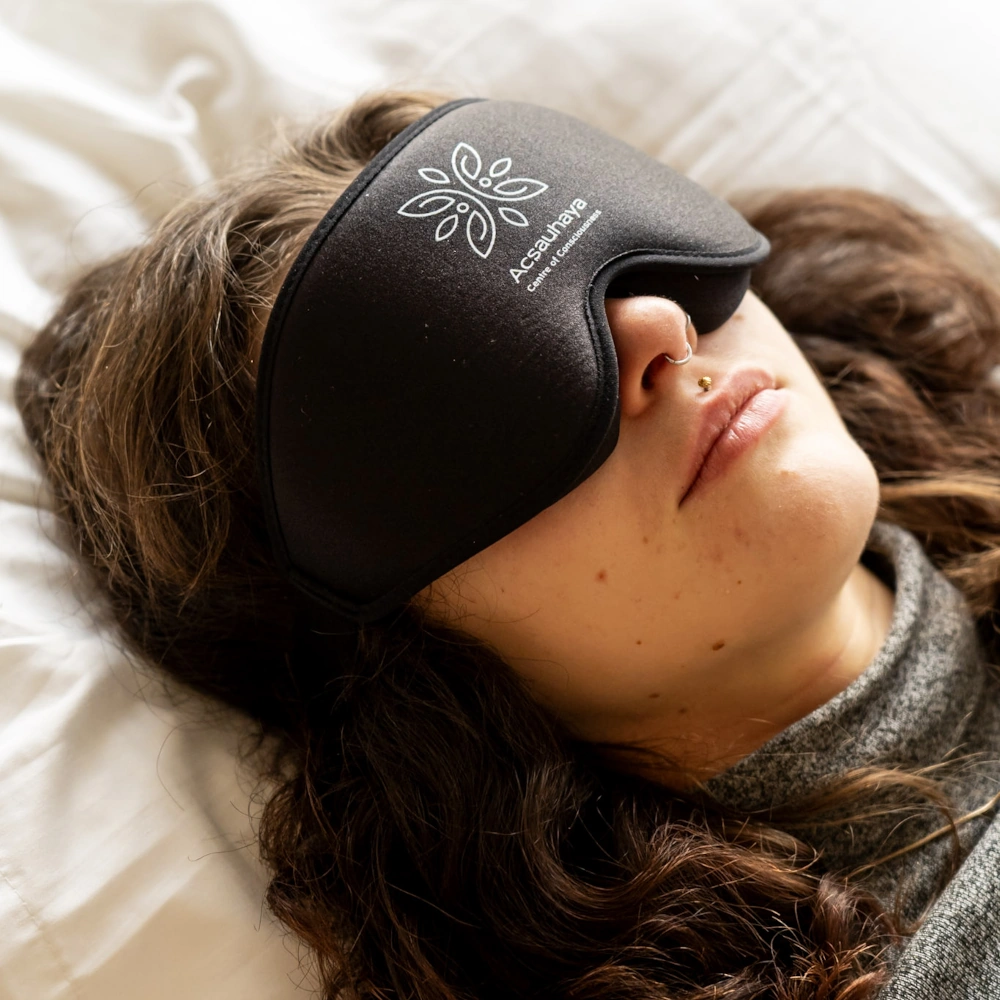 Young woman with black blindfold laying on white pillow, Acsauhaya logo on blindfold